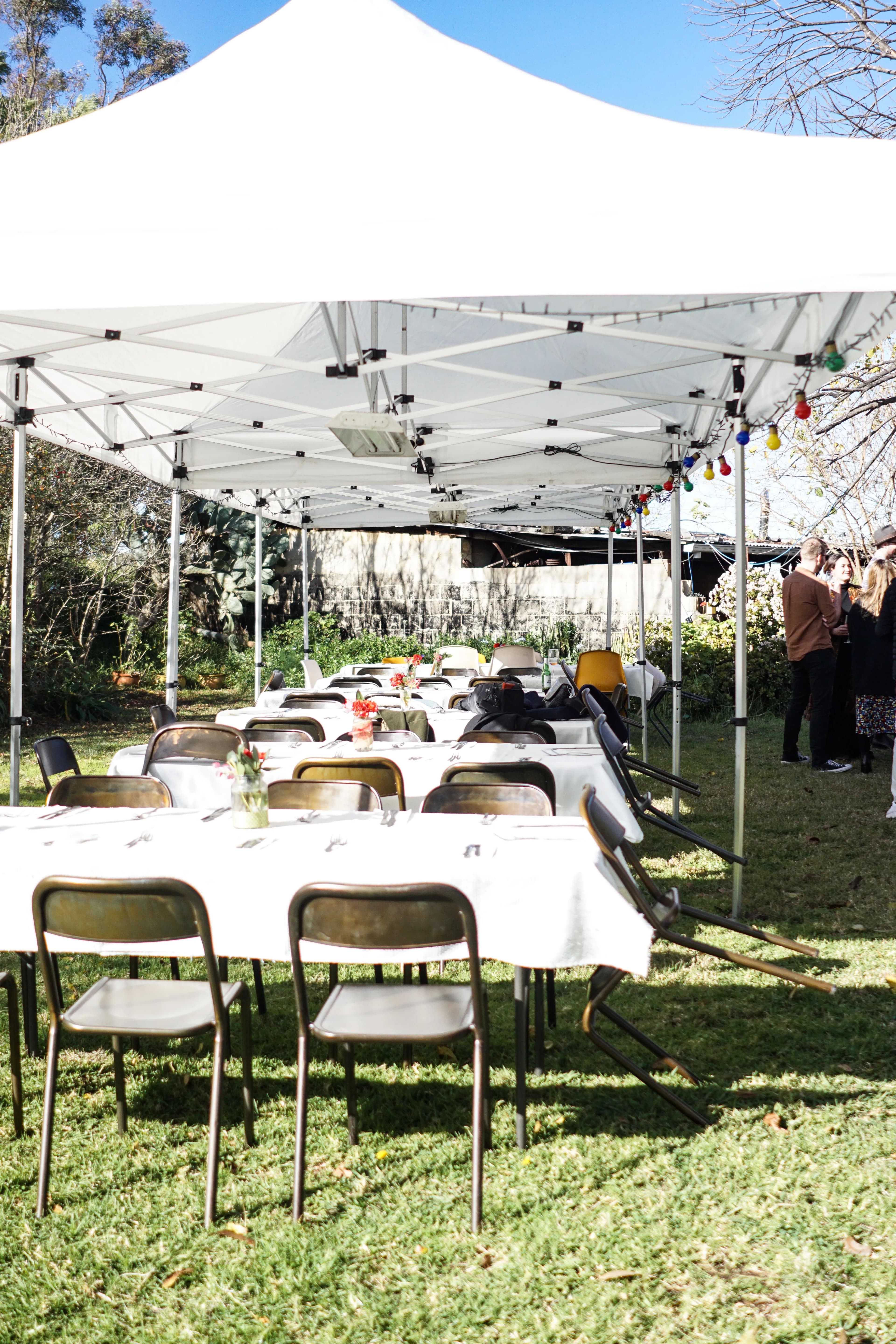 Pop-up canopy tents over long dining tables, strung with coloured globe lights